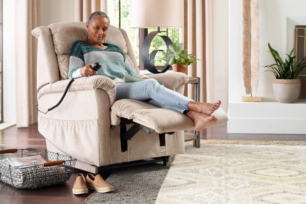 Woman in a light tan colored lift chair using the remote to pull out the footrest