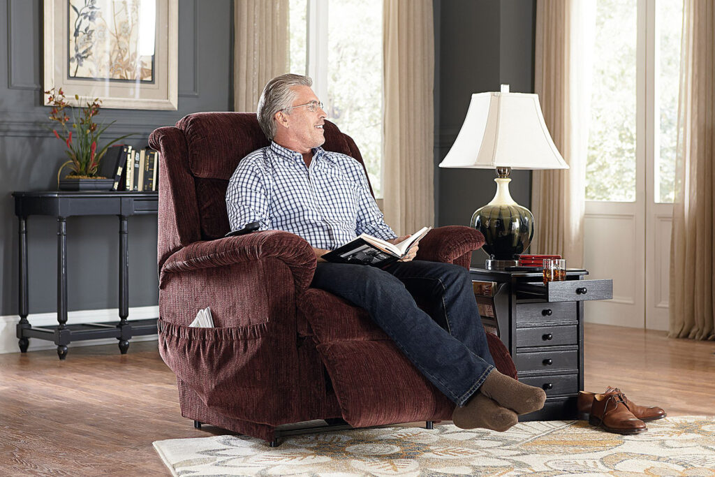 Man in a red textured lift chair smiling while reading a book