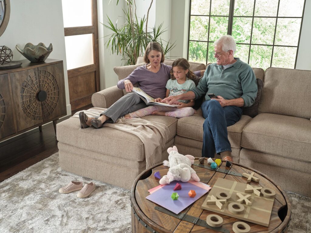 Grandparents and grandchild on a sectional sofa reading a book